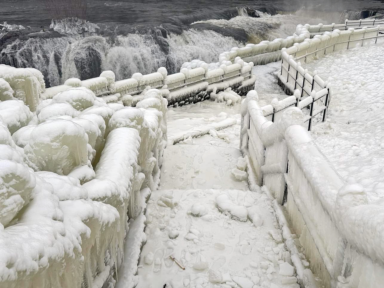 An ice-encased walkway and railings generated from spray from Great Falls (background) in Paterson (Passaic County) during the cold January outbreak (photo courtesy of Liz Reilly).